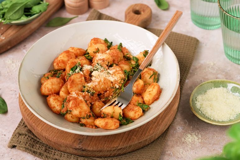 Gnocchi z czerwonym pesto na talerzu, obok w miseczce parmezan
