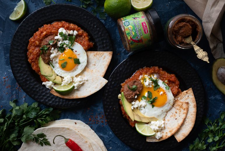 Huevos Rancheros czyli jajka po farmersku na czarnym talerzu, obok na stole tortille, natka pietruszki, chilli i pasta fasolowa od Helcom ethnic w słoiku