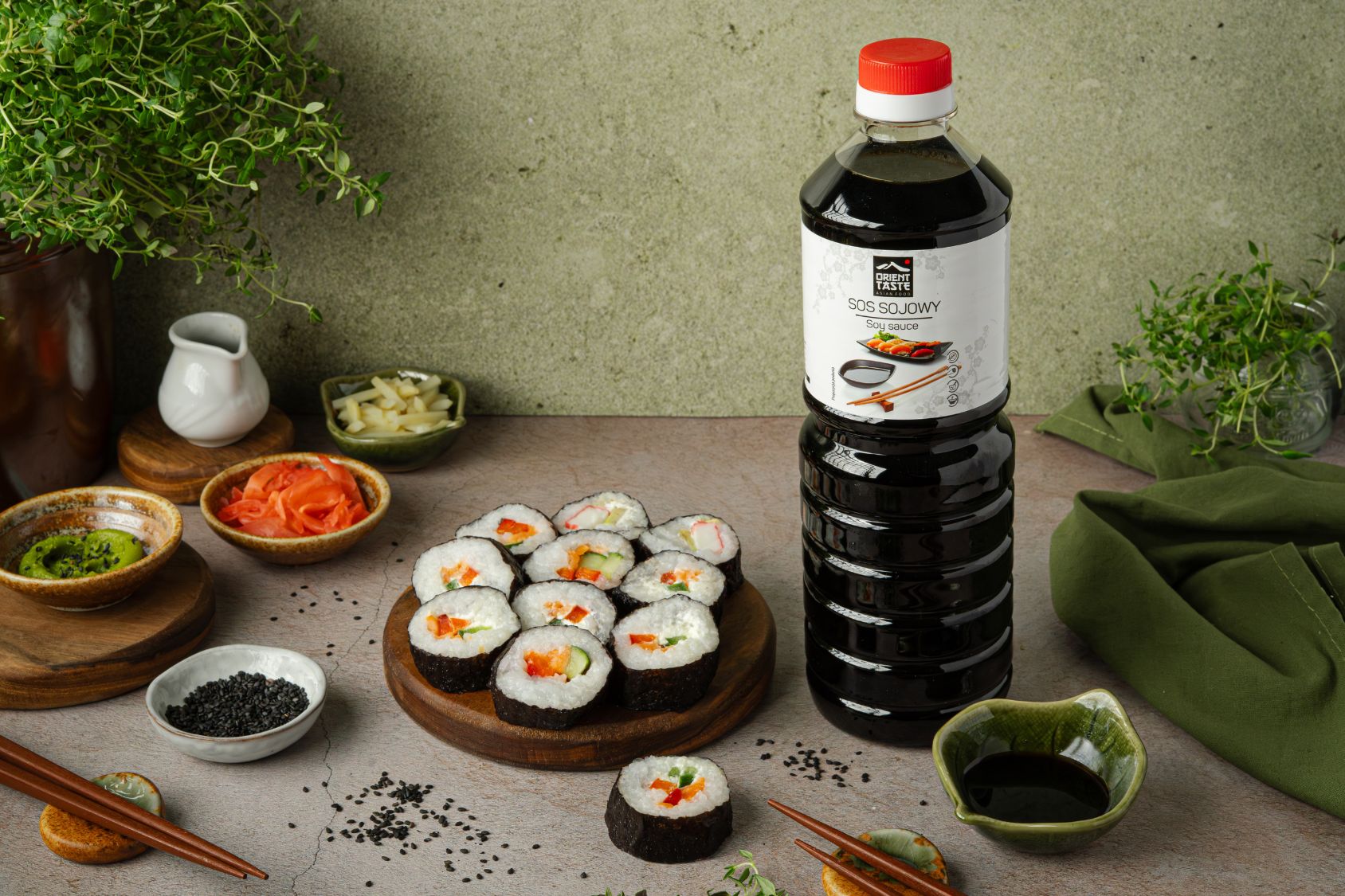 Kawałki sushi na drewnianej desce, obok sos sojowy od Orient Taste, miseczki z sosem sojowym, wakame, imbirem w plastrach